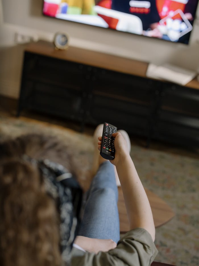 A woman relaxes on a couch inside her cozy home, watching television with a remote in hand.